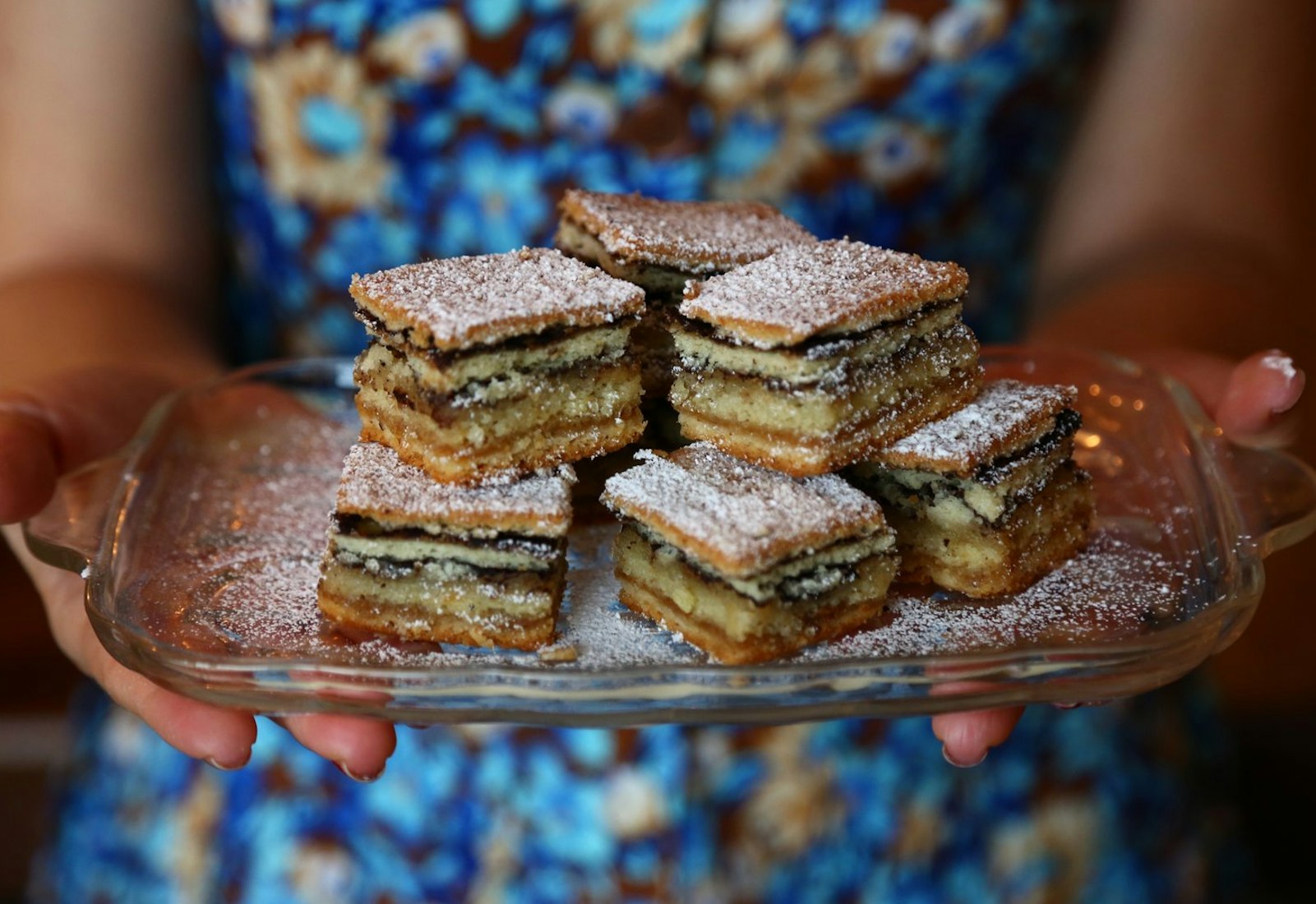 Person holding dish with servings of German layer cake sprinkled with powdered sugar.