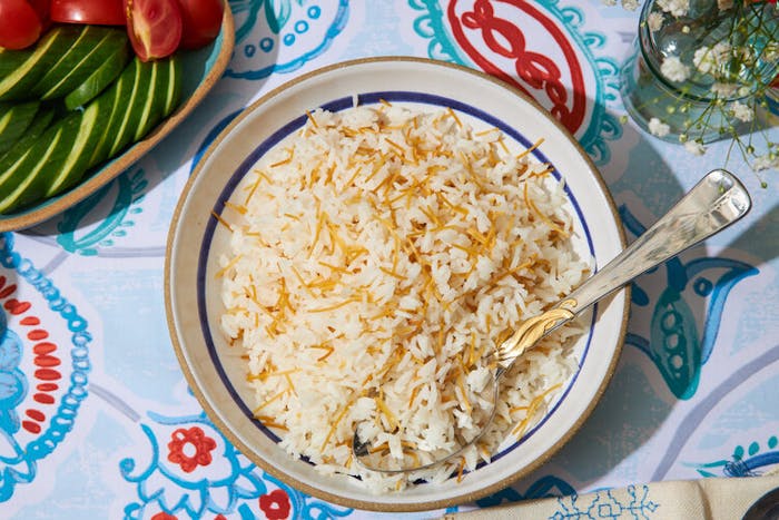 Arroz con fideos, sliced cucumber and tomato, fresh flowers atop blue and red tablecloth.