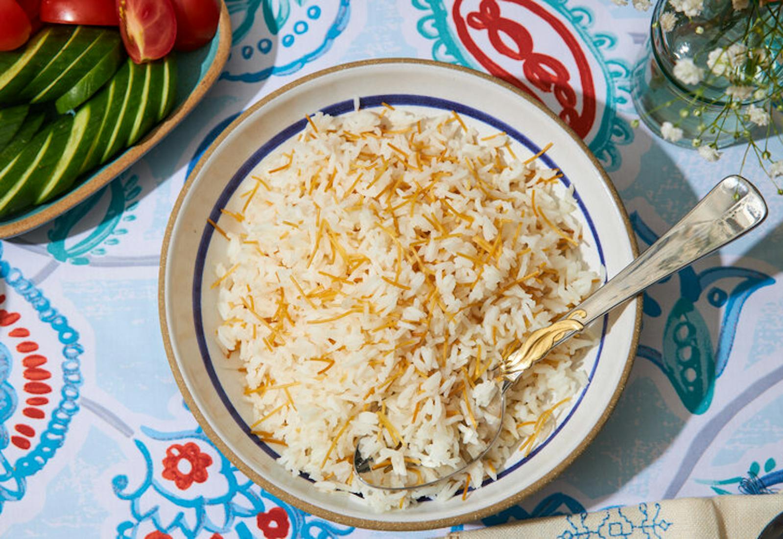 Arroz con fideos, sliced cucumber and tomato, fresh flowers atop blue and red tablecloth.