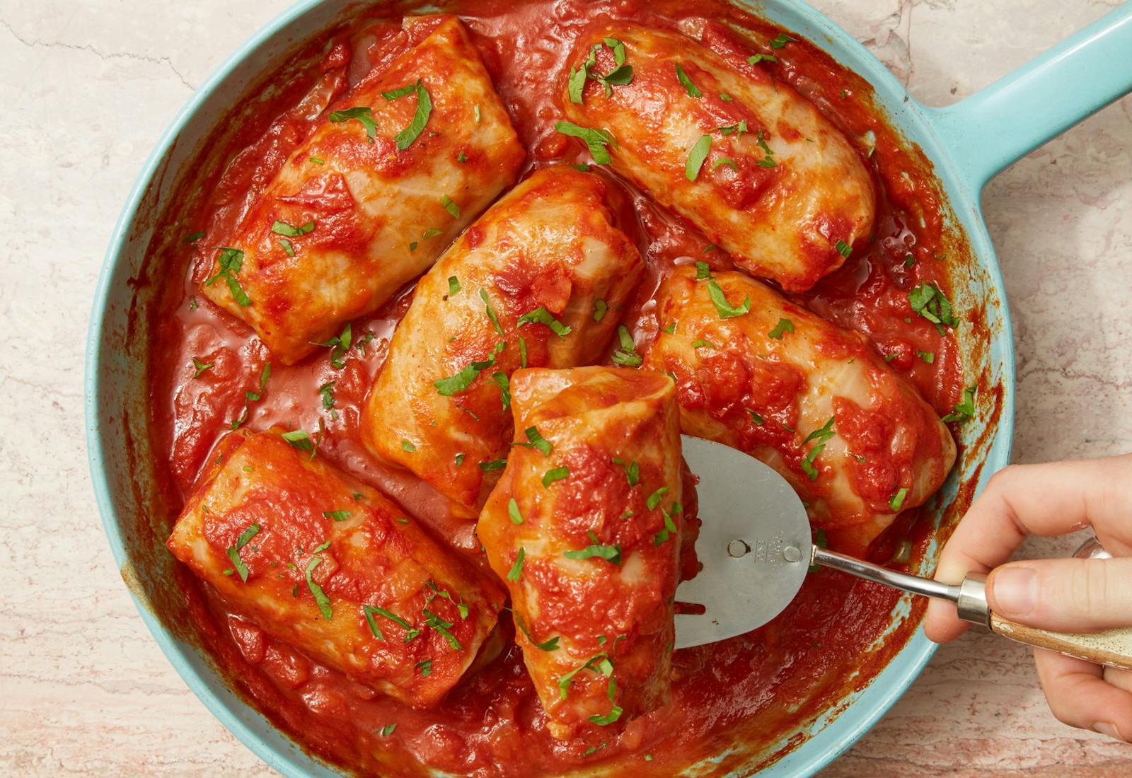Blue skillet with stuffed cabbage in tomato sauce garnished with parsley.