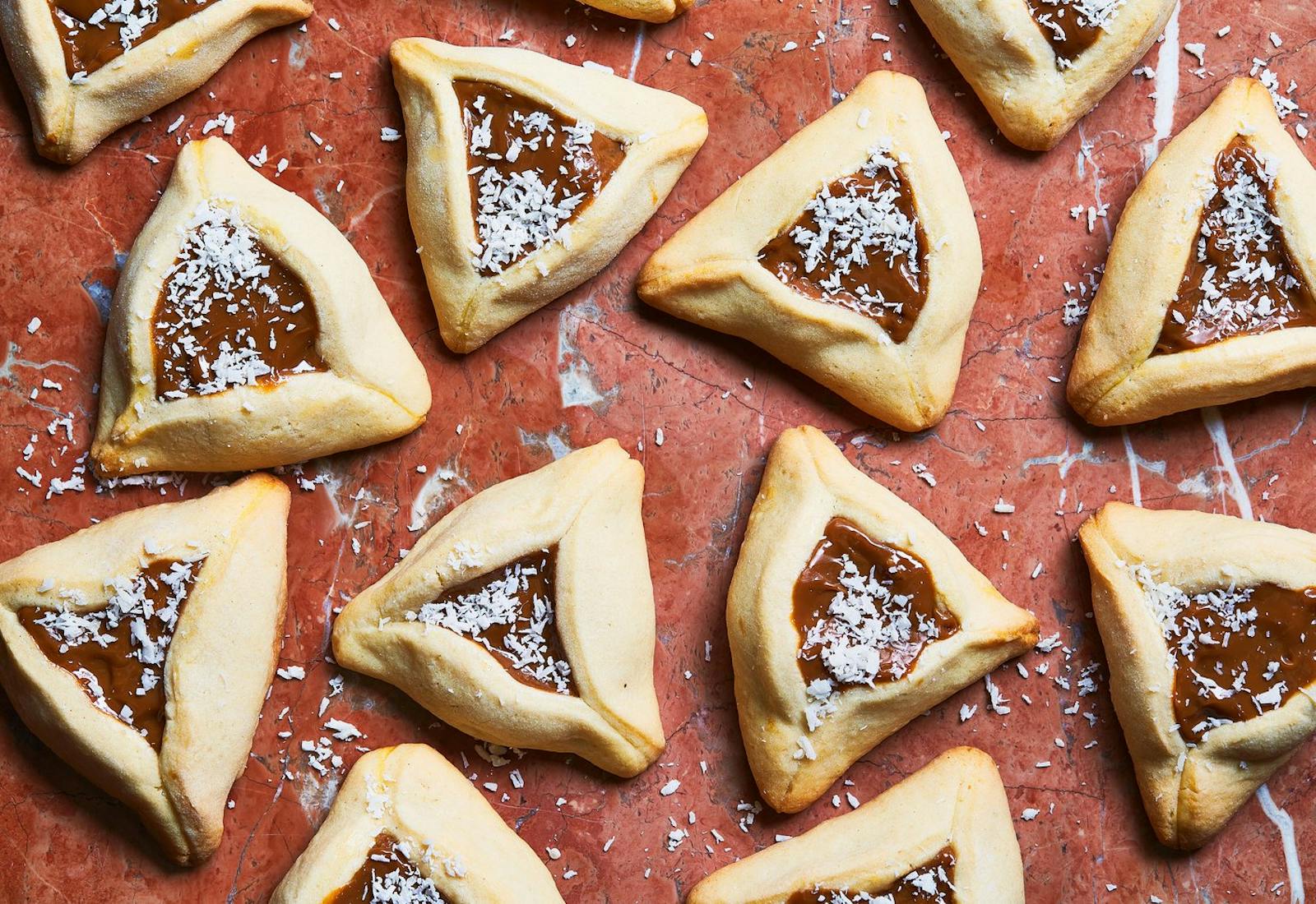 Hamantaschen with coconut flakes atop red surface.