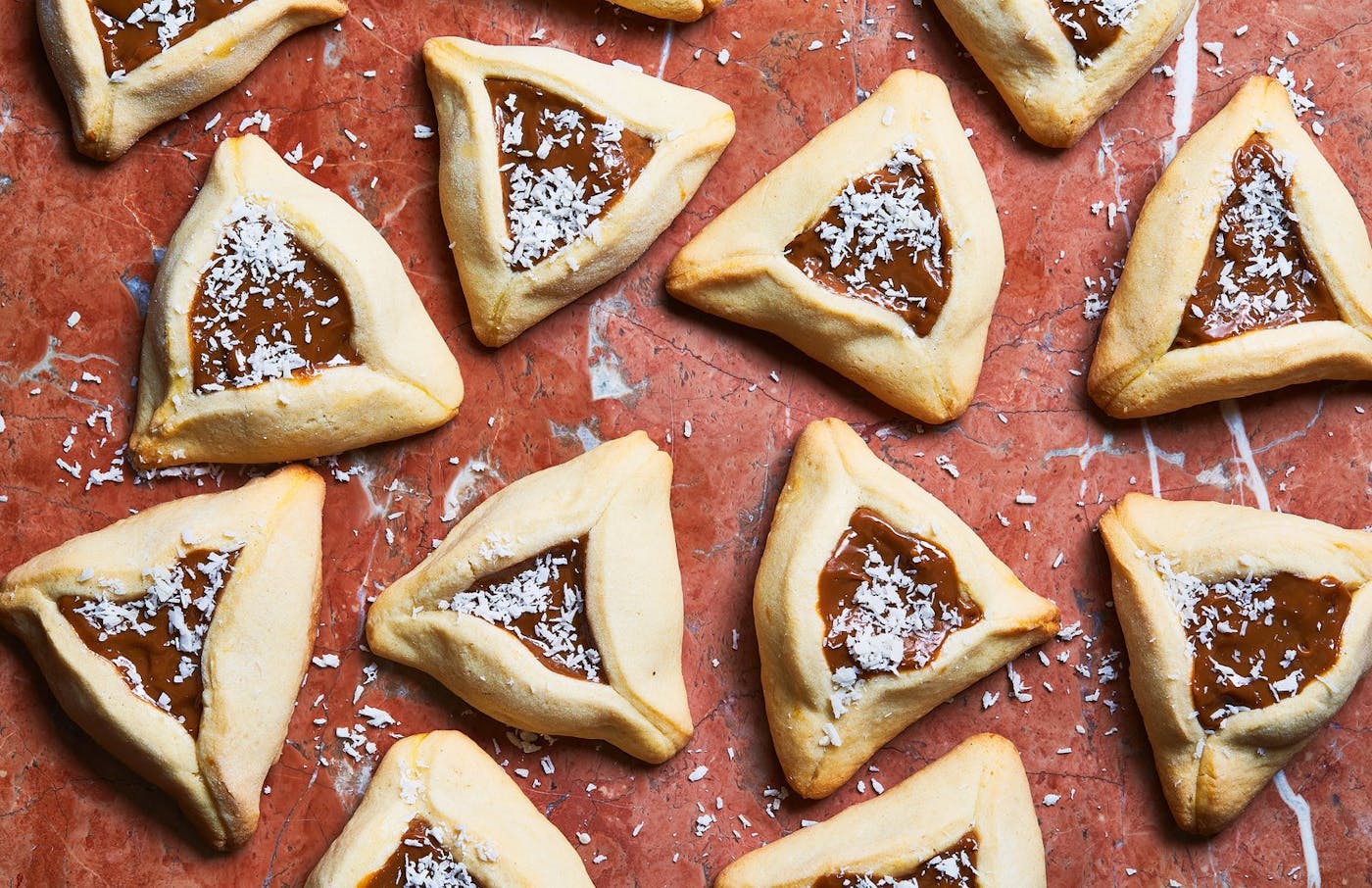 Hamantaschen with coconut flakes atop red surface.