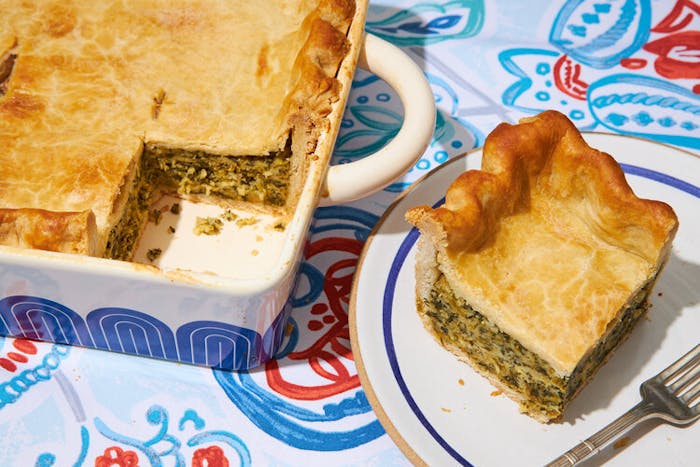 Torta de Espinaca in blue casserole dish, small plate with slice of torta atop blue and red tablecloth.