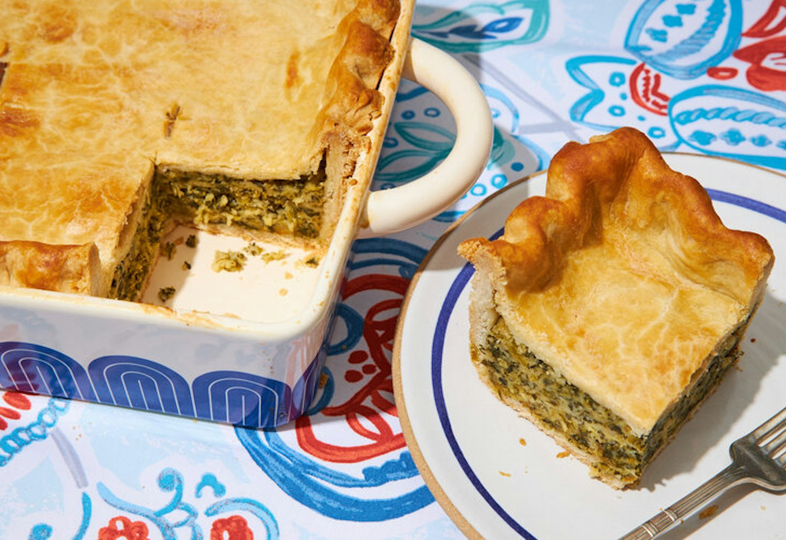 Torta de Espinaca in blue casserole dish, small plate with slice of torta atop blue and red tablecloth.
