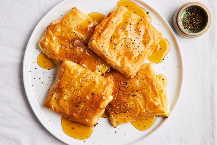 Phyllo bundles with honey and cracked black pepper on white plate atop white surface. 