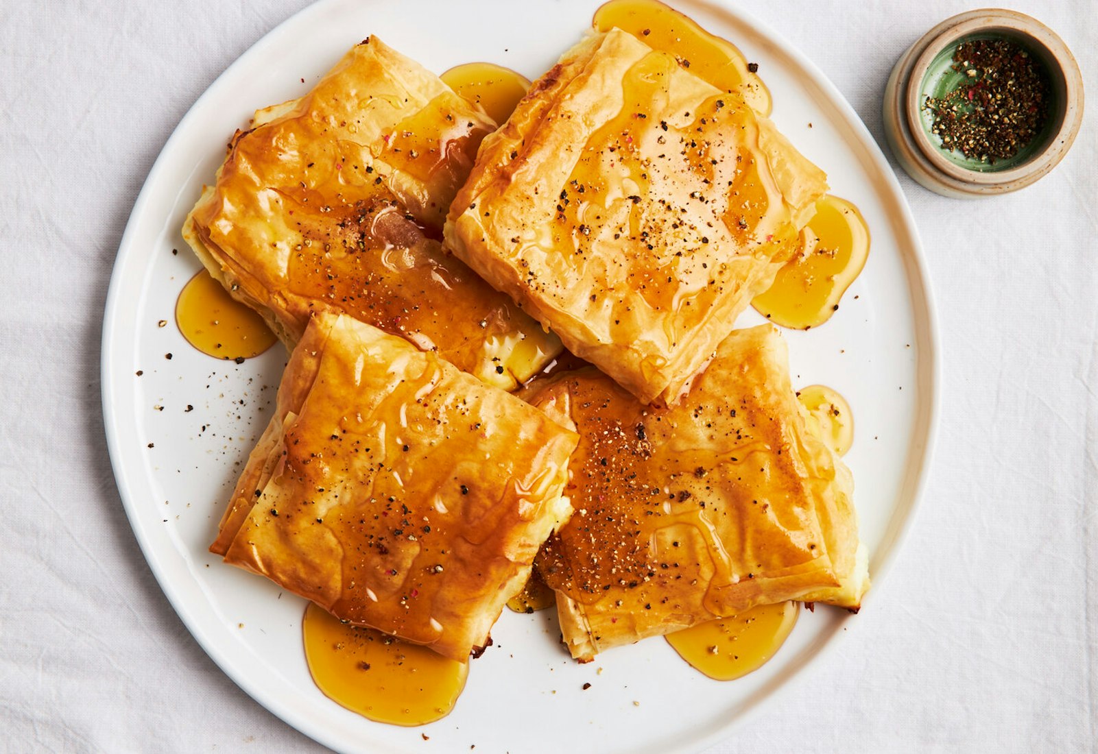Phyllo bundles with honey and cracked black pepper on white plate atop white surface. 