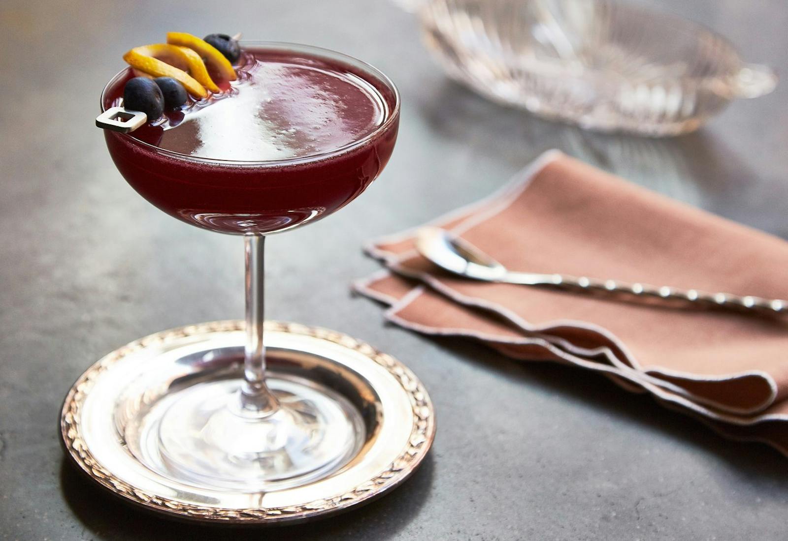 Blueberry cocktail garnished with blueberries and lemon slices, atop black surface.