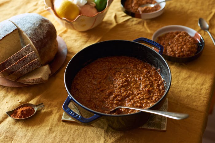 Messer wot in cast iron pot, sliced dabo bread, dish with berbere spice atop yellow tablecloth.