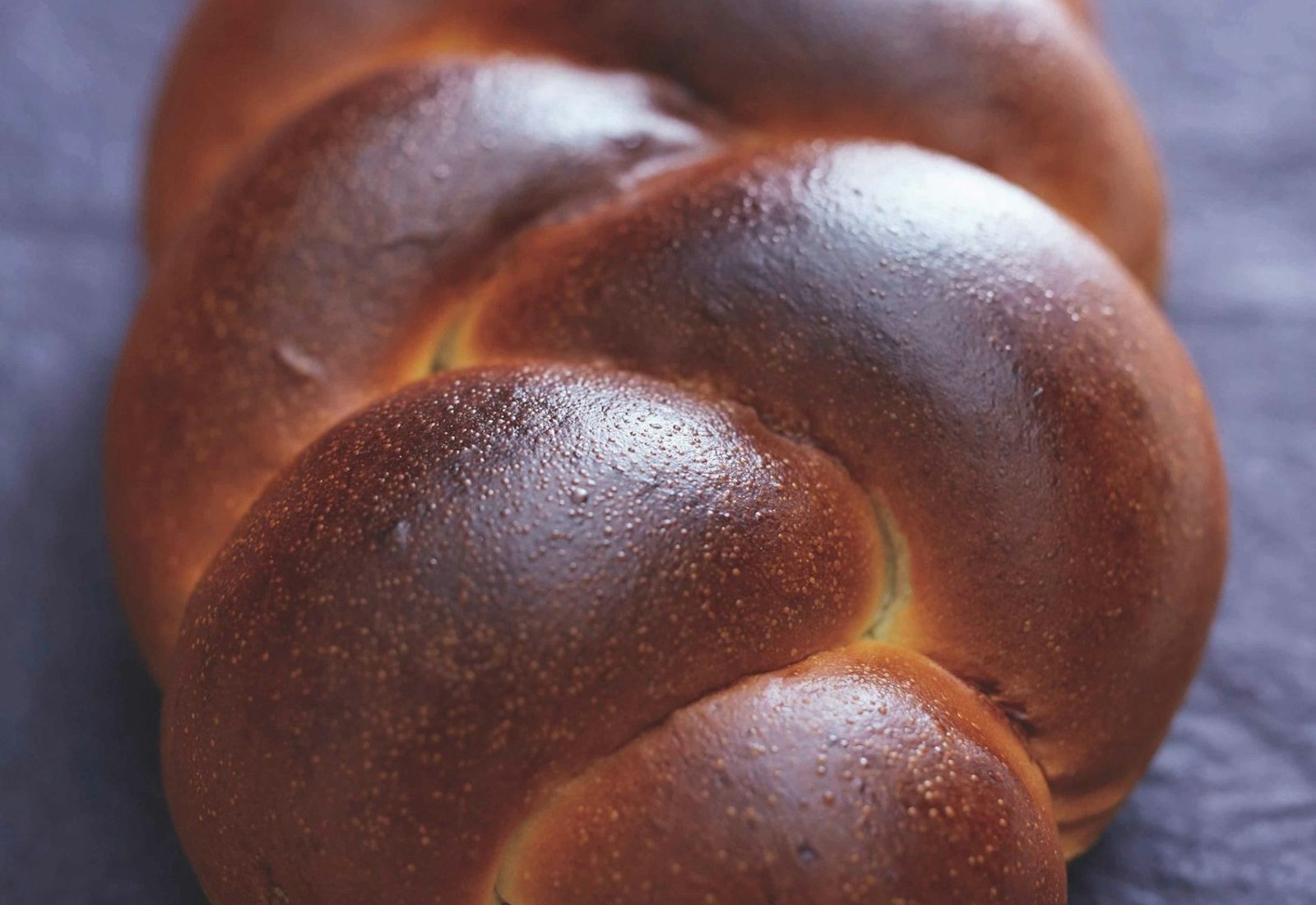 Golden braided challah atop navy tablecloth.