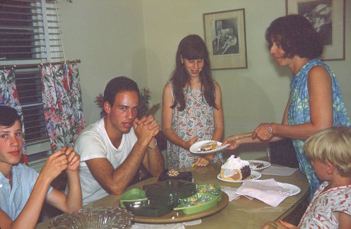 Stern siblings around dining table as mother serves ice cream cake.