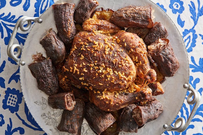 Roasted chicken surrounded by stuffed eggplants on large tray atop blue floral tablecloth.