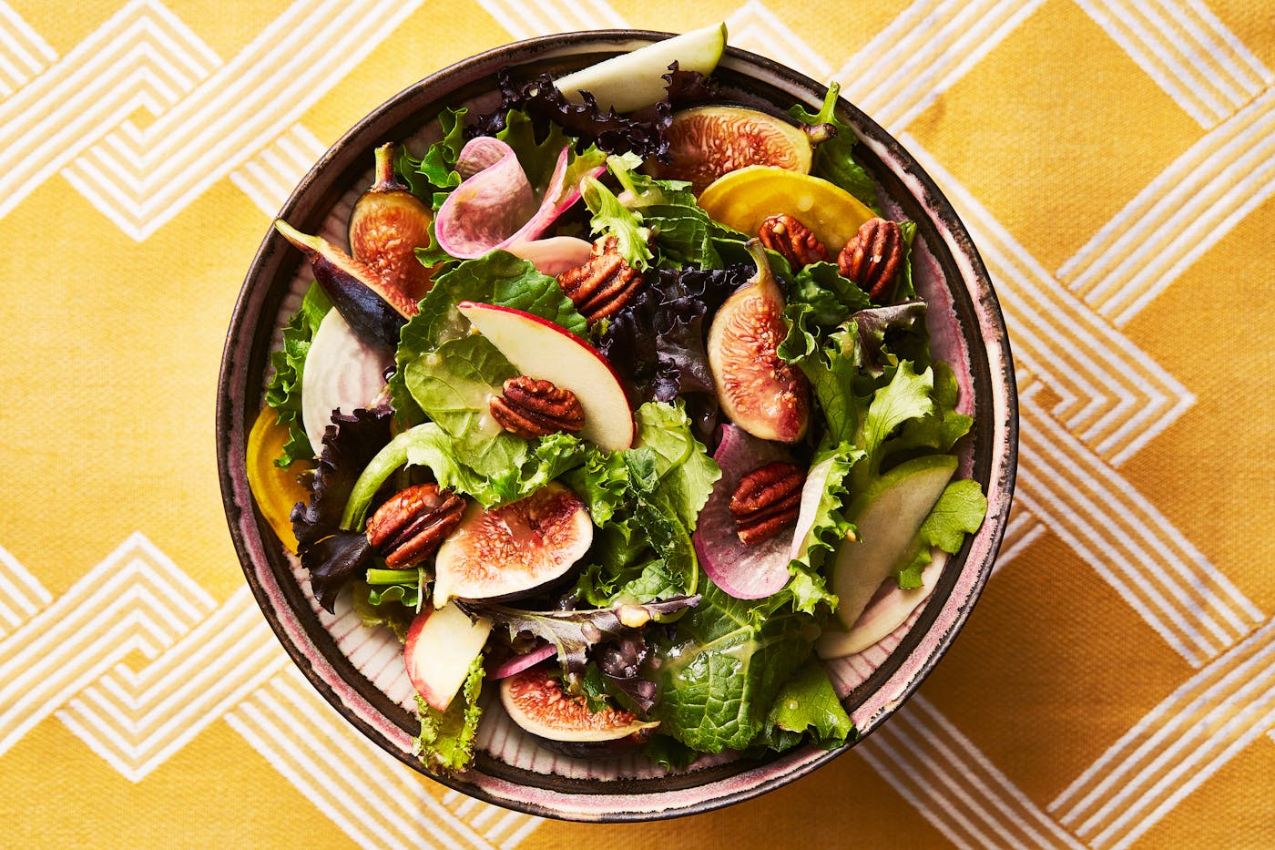 Apple, honey, and fig salad in serving bowl atop yellow tablecloth.