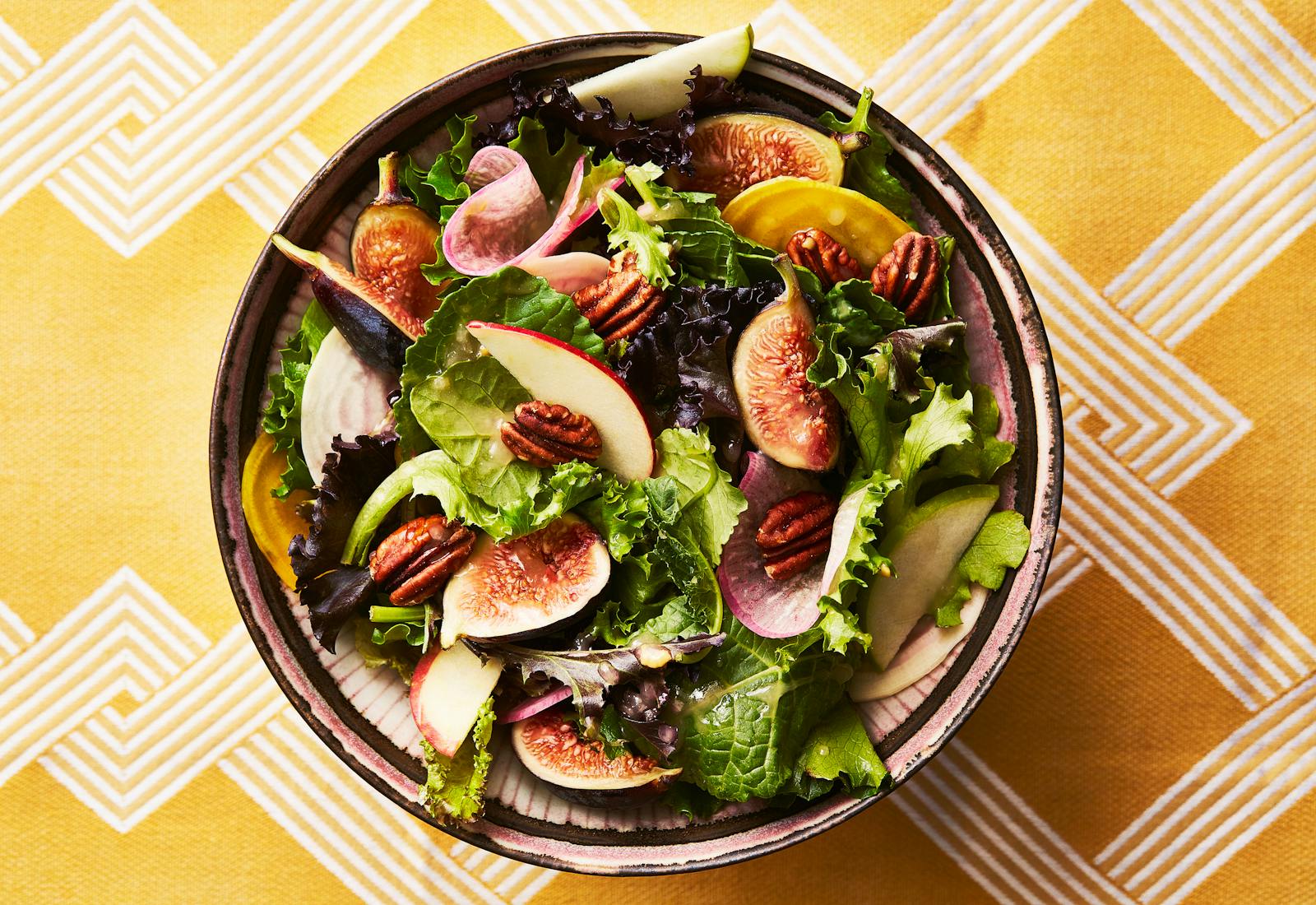 Apple, honey, and fig salad in serving bowl atop yellow tablecloth.