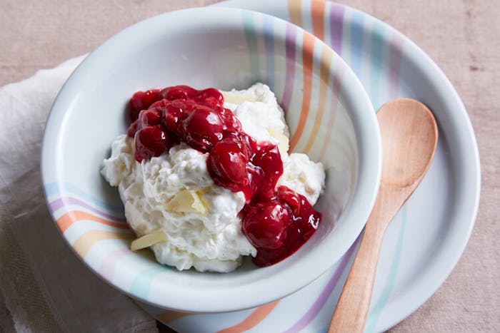 Rice pudding with slivered almond and cherry sauce in colorful bowl with wooden serving spoon.