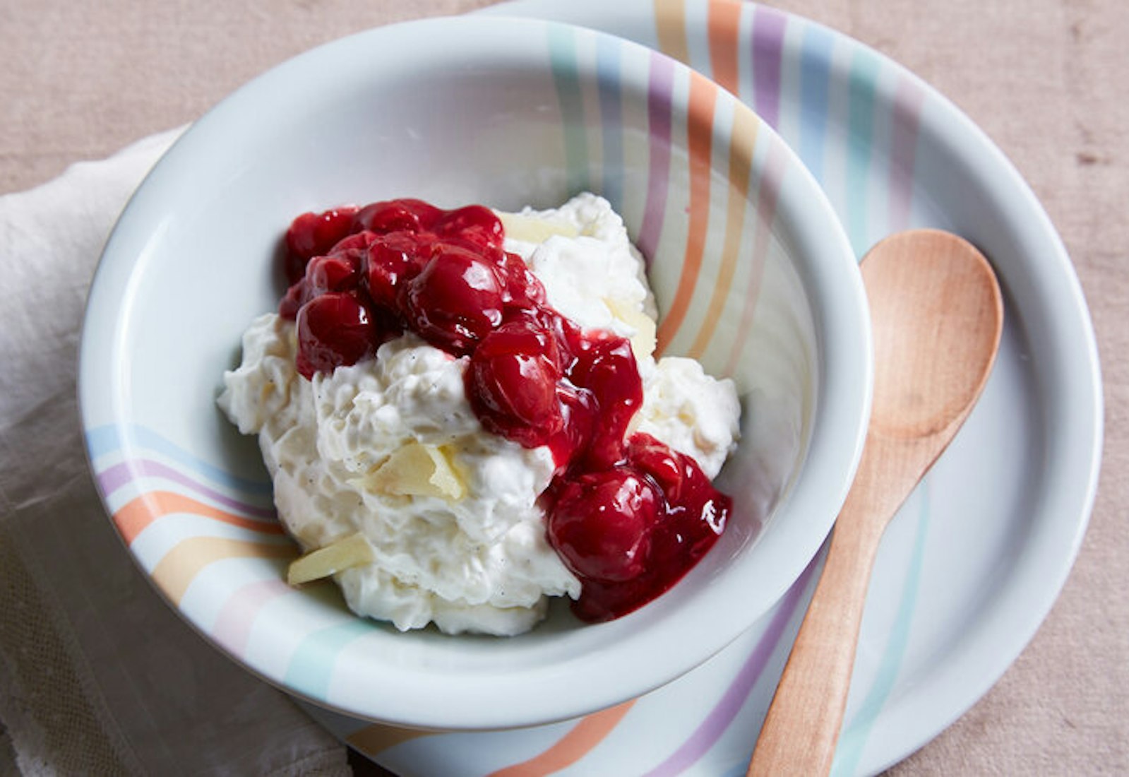 Rice pudding with slivered almond and cherry sauce in colorful bowl with wooden serving spoon.