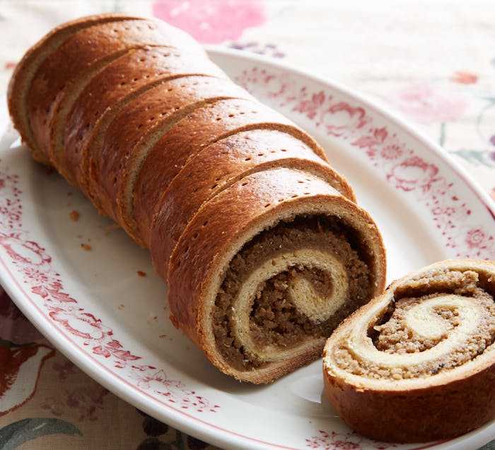 Sliced beigli on white dish with red floral patterns, atop floral tablecloth.