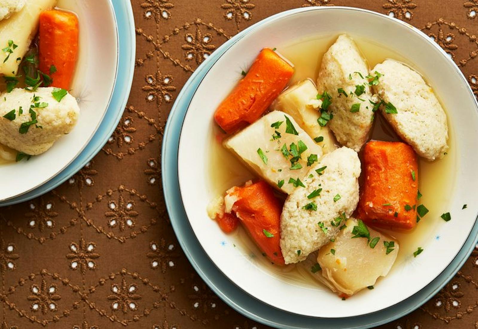 Two bowls of soup with chopped parsley atop brown surface. 