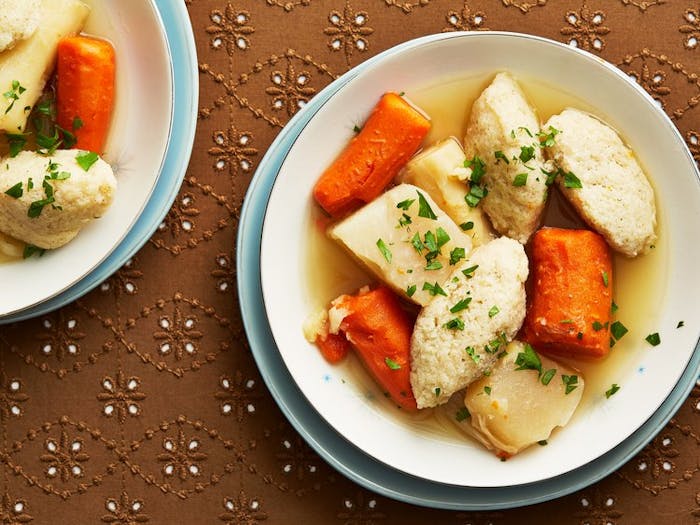 Two bowls of soup with chopped parsley atop brown surface. 