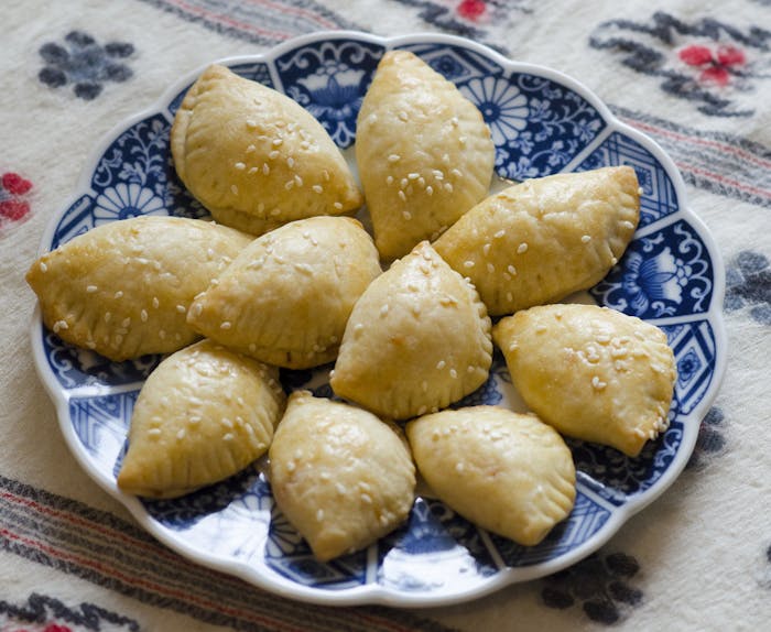 Cheese sambusak with sesame seeds on blue scalloped dish atop woven tablecloth.