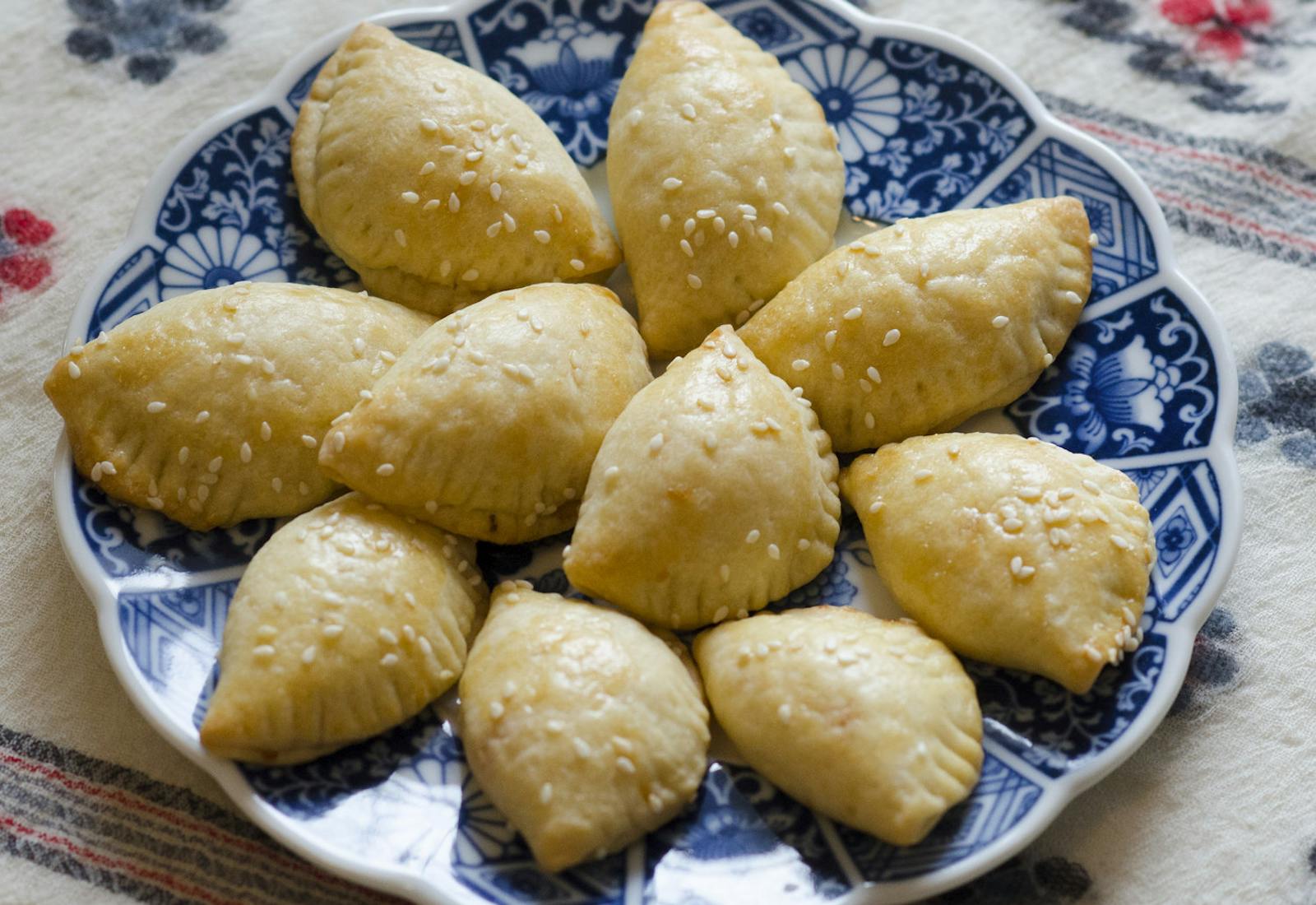 Cheese sambusak with sesame seeds on blue scalloped dish atop woven tablecloth.