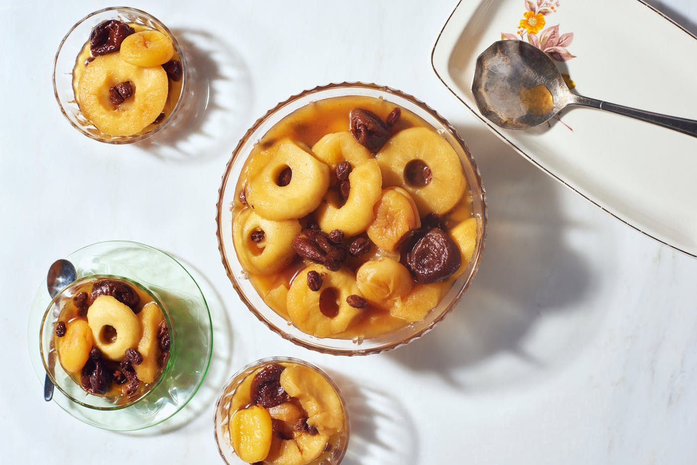 Large and small glass bowls with dried fruit compote atop white surface.
