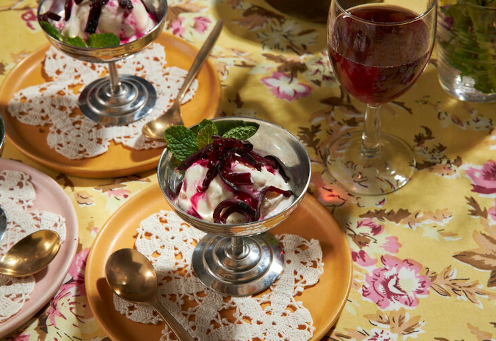 Ice cream with beets and mint in metal coupes, red wine atop yellow floral tablecloth.