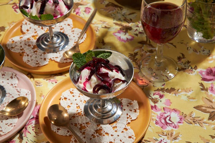 Ice cream with beets and mint in metal coupes, red wine atop yellow floral tablecloth.