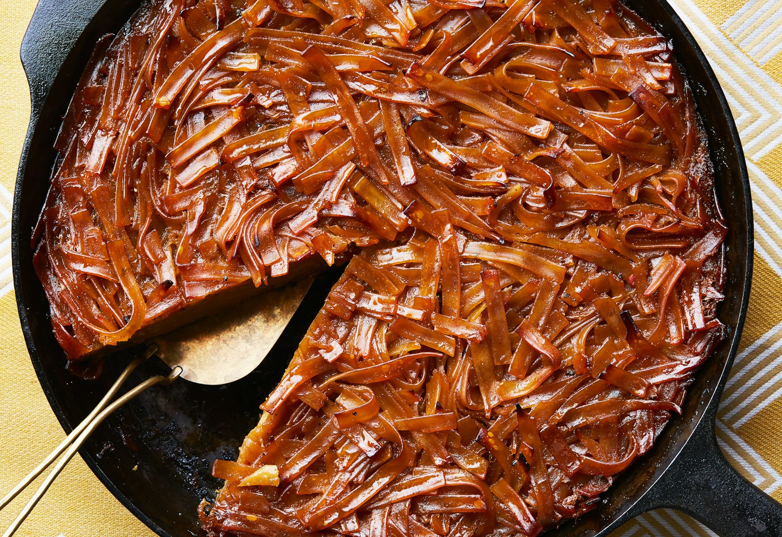 Kugel in cast iron pan atop yellow tablecloth.