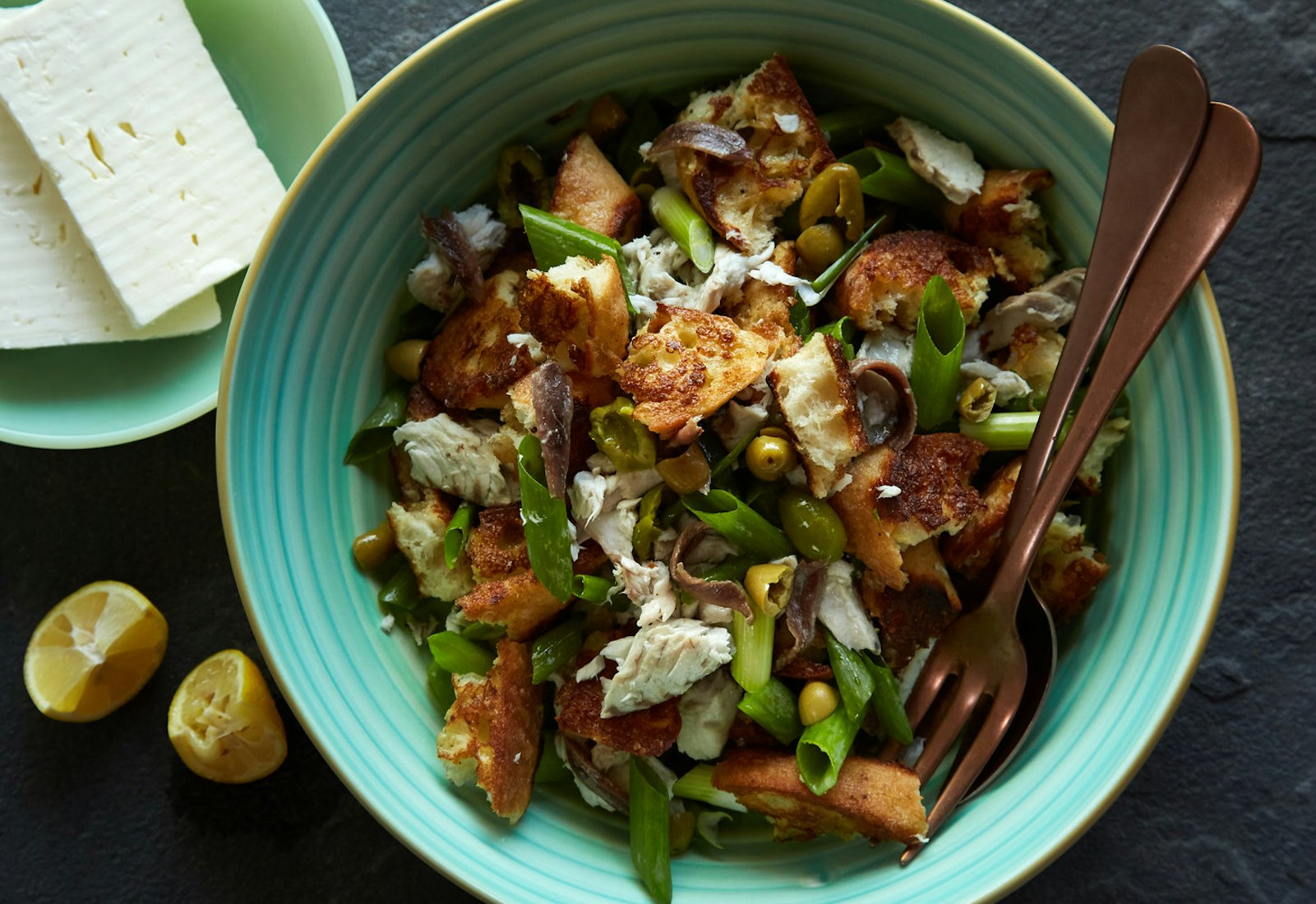 Fish panzanella in blue bowl alongside lemon wedges and bulgarian feta.