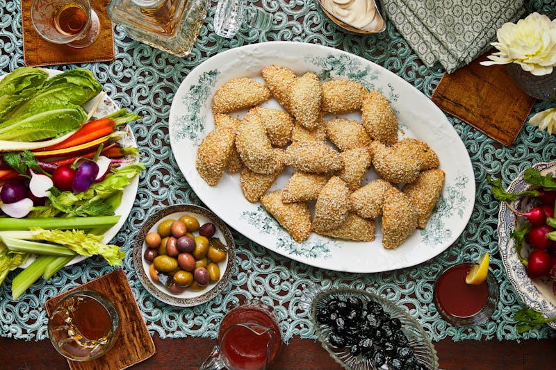 Serving platter of sambusak with a bowl of olives and a plate of crudite.