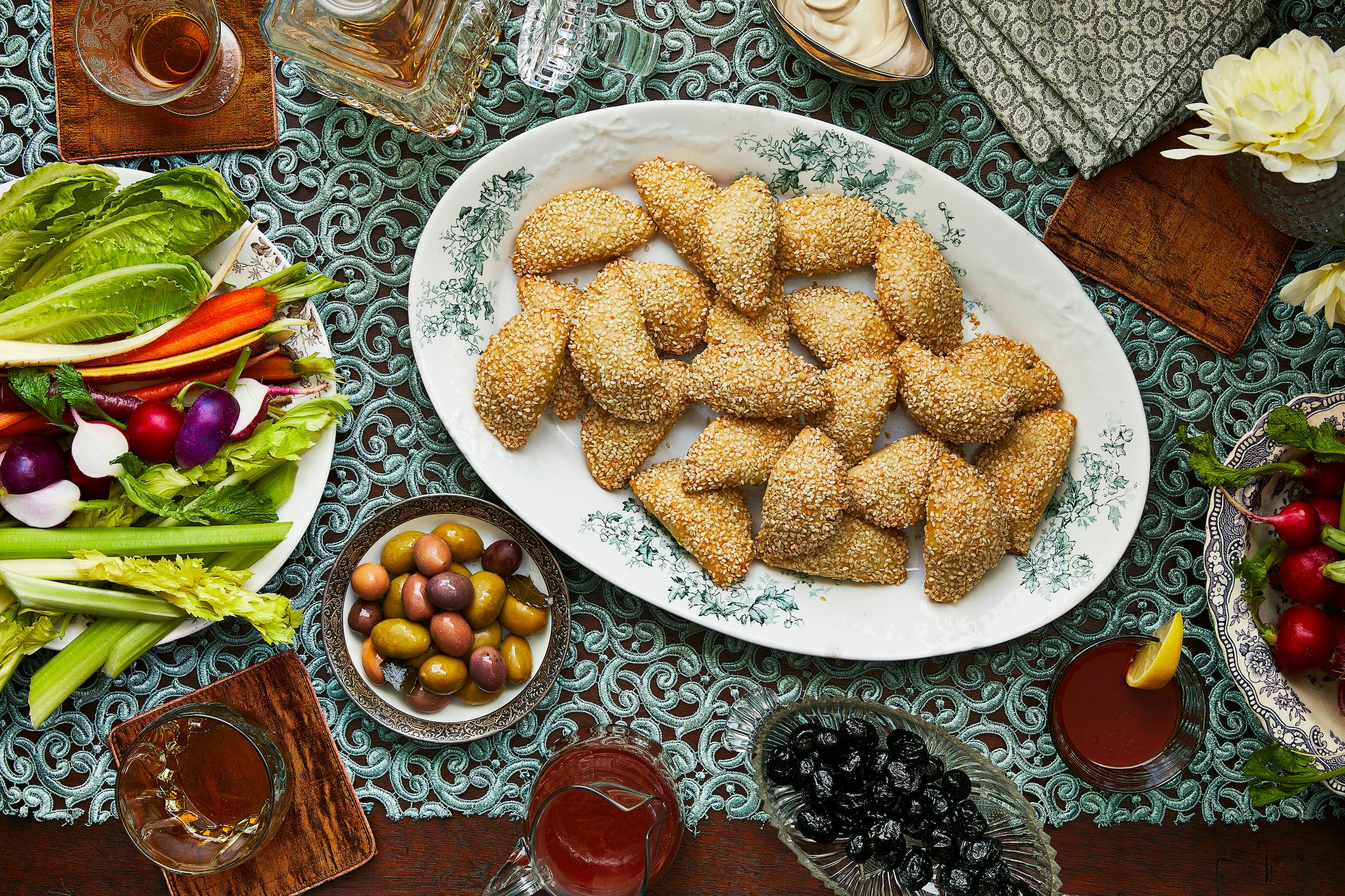 Serving platter of sambusak with a bowl of olives and a plate of crudite.