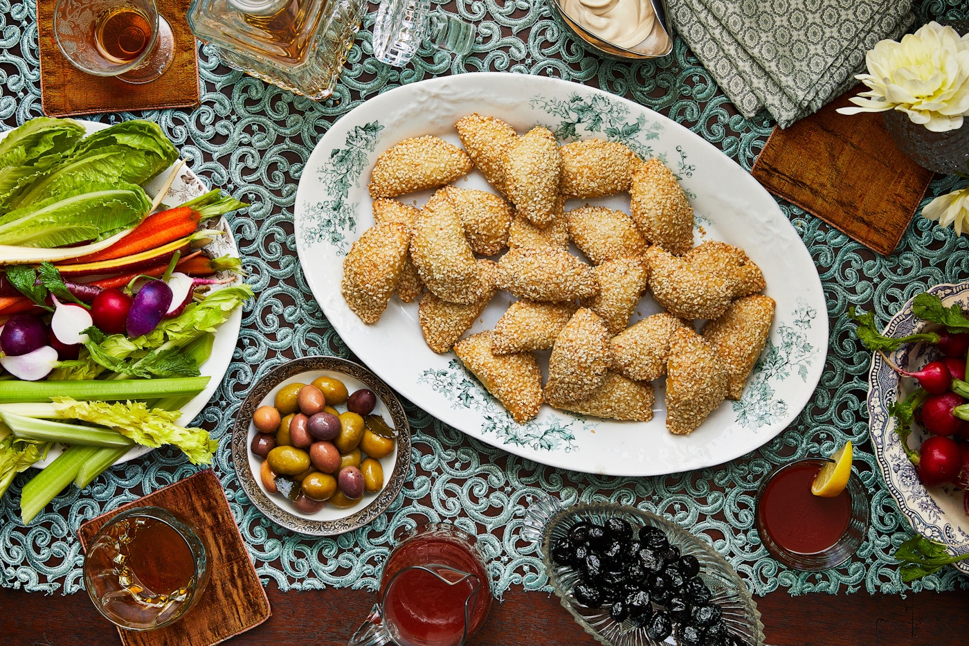 Serving platter of sambusak with a bowl of olives and a plate of crudite.