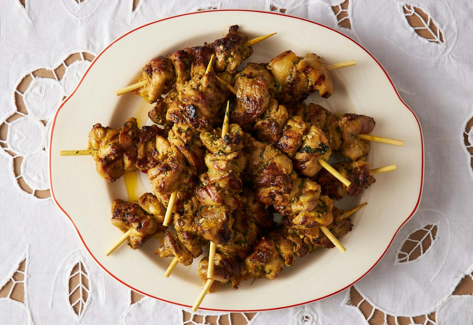 Grilled chicken skewers atop white floral tablecloth. 
