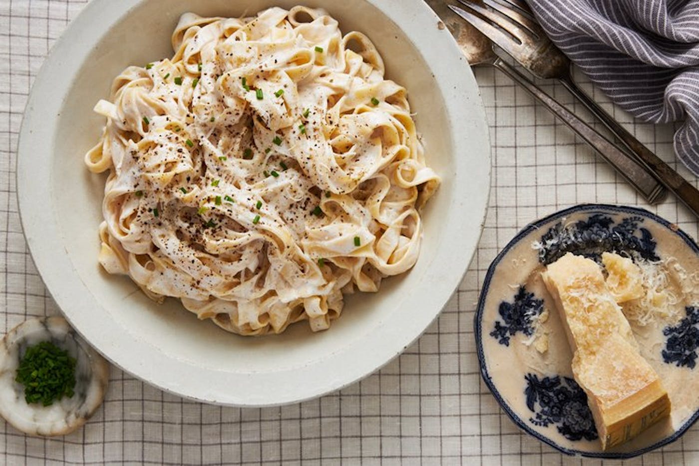 Noodles with cottage cheese, sprinkled with fresh chives, cracked black pepper and parmesan atop checkered tablecloth.