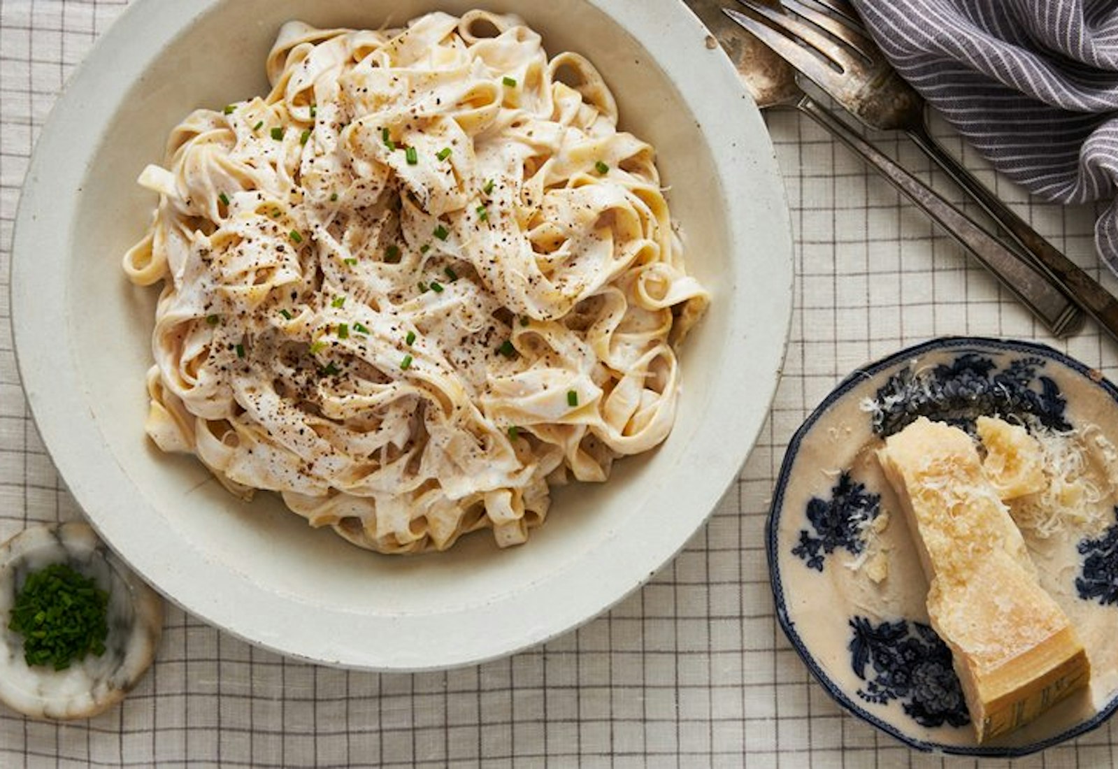 Noodles with cottage cheese, sprinkled with fresh chives, cracked black pepper and parmesan atop checkered tablecloth.