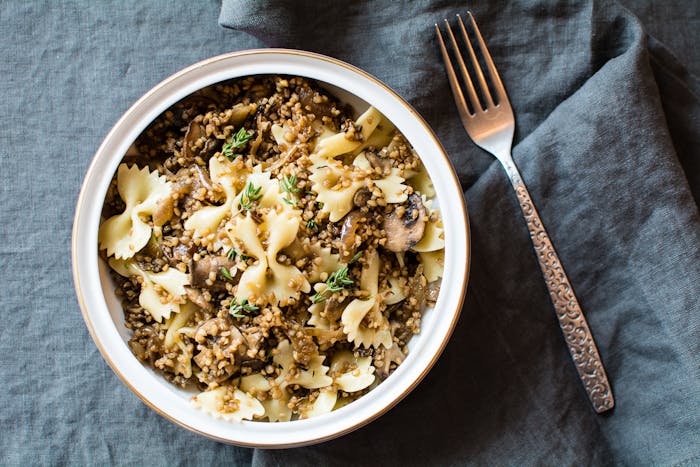 Kasha varnishes with mushrooms sprinkled with fresh thyme in white bowl atop grey cloth.
