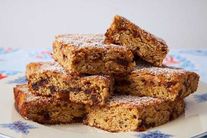 Squares of torta de dateless sprinkled with powdered sugar on blue floral plate.