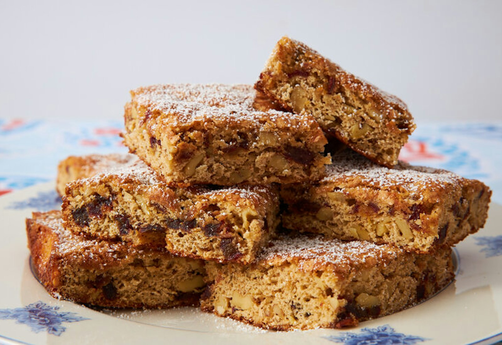 Squares of torta de dateless sprinkled with powdered sugar on blue floral plate.