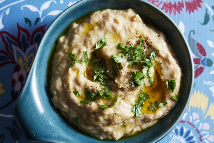 Fumaça with olive oil, parsley and cracked black pepper in blue bowl atop blue floral tablecloth.