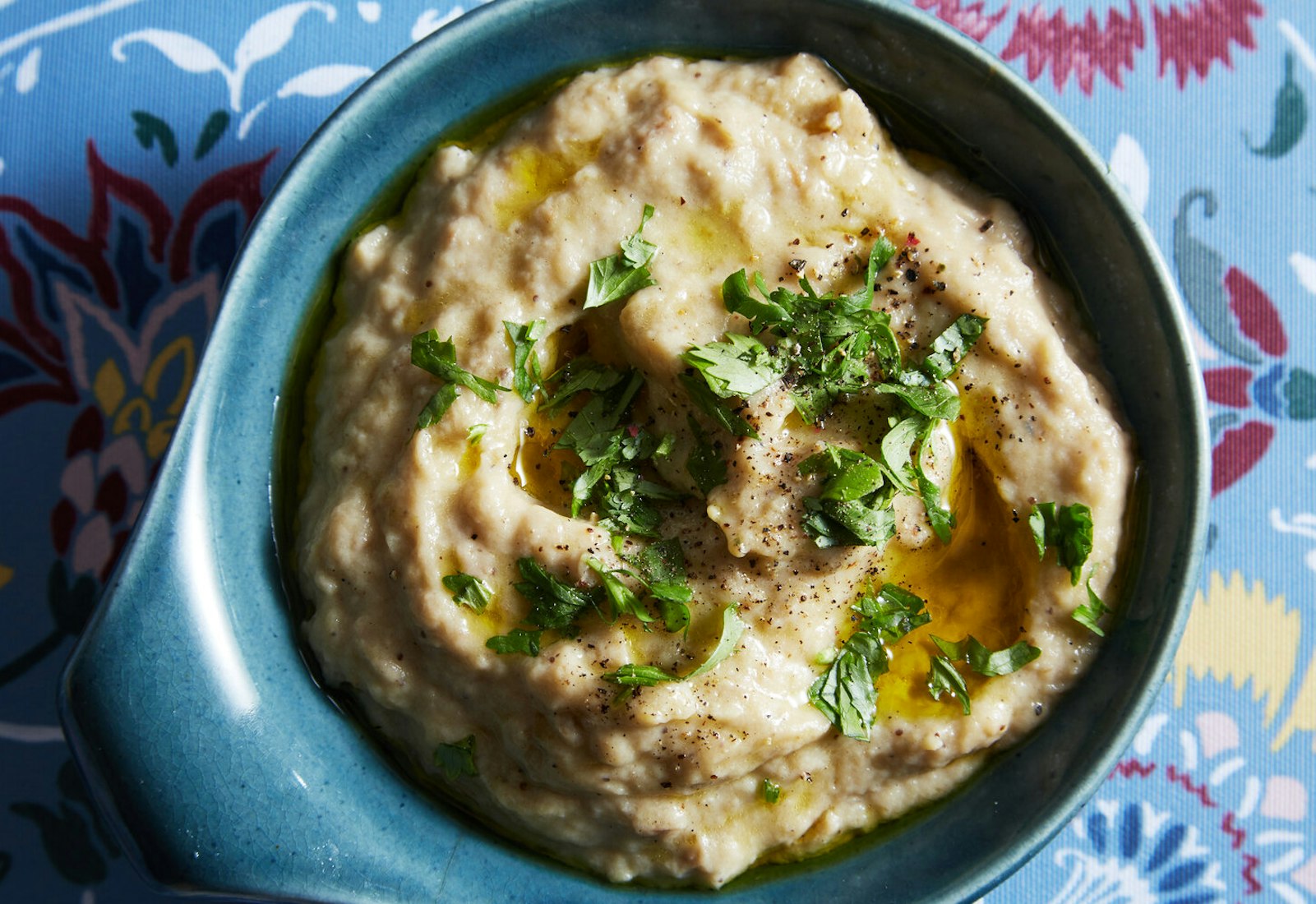 Fumaça with olive oil, parsley and cracked black pepper in blue bowl atop blue floral tablecloth.