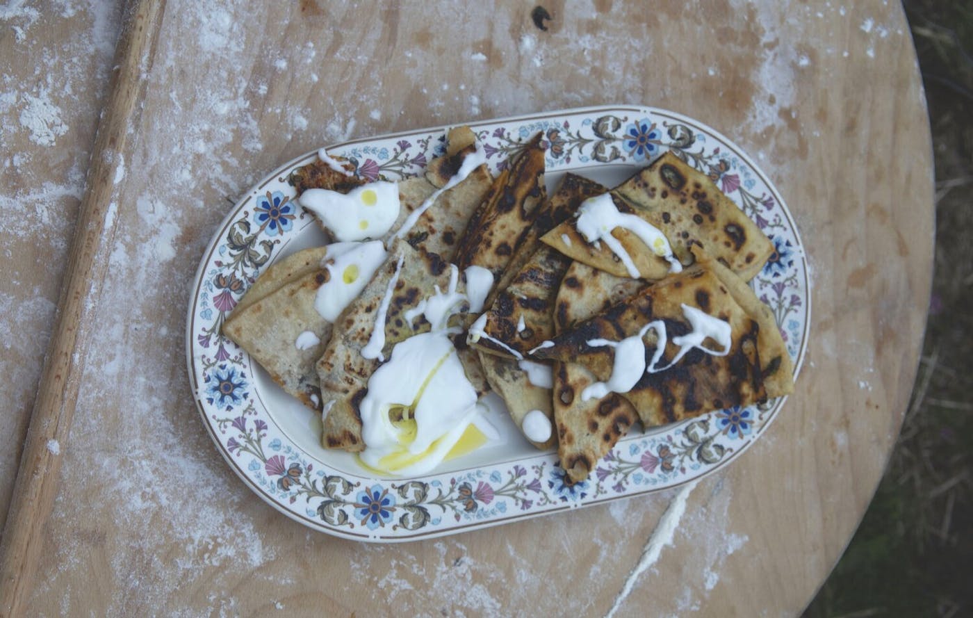 Pita with drizzle of yogurt and olive oil on floral tray, atop wooden surface.