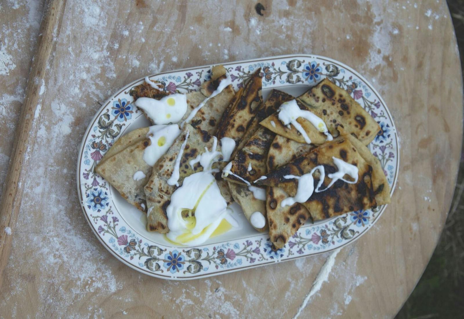 Pita with drizzle of yogurt and olive oil on floral tray, atop wooden surface.