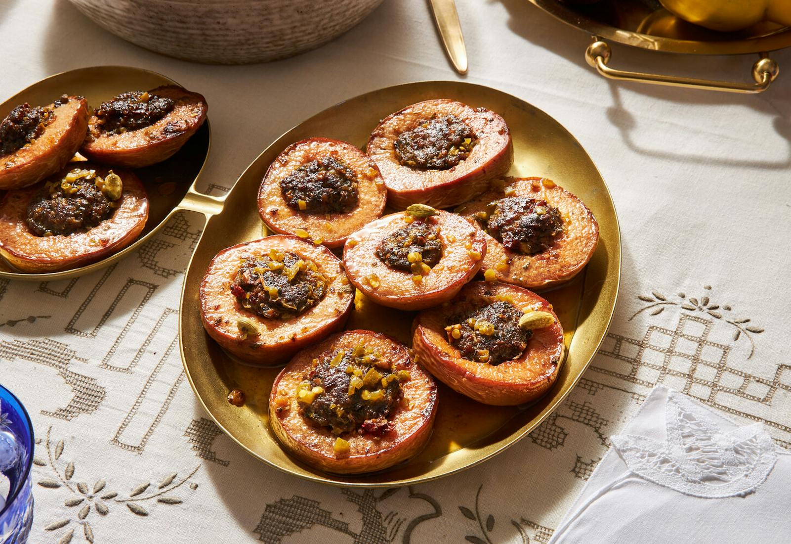 Dolmeh beh on gold platter with platter of fresh quince atop white patterned tablecloth.
