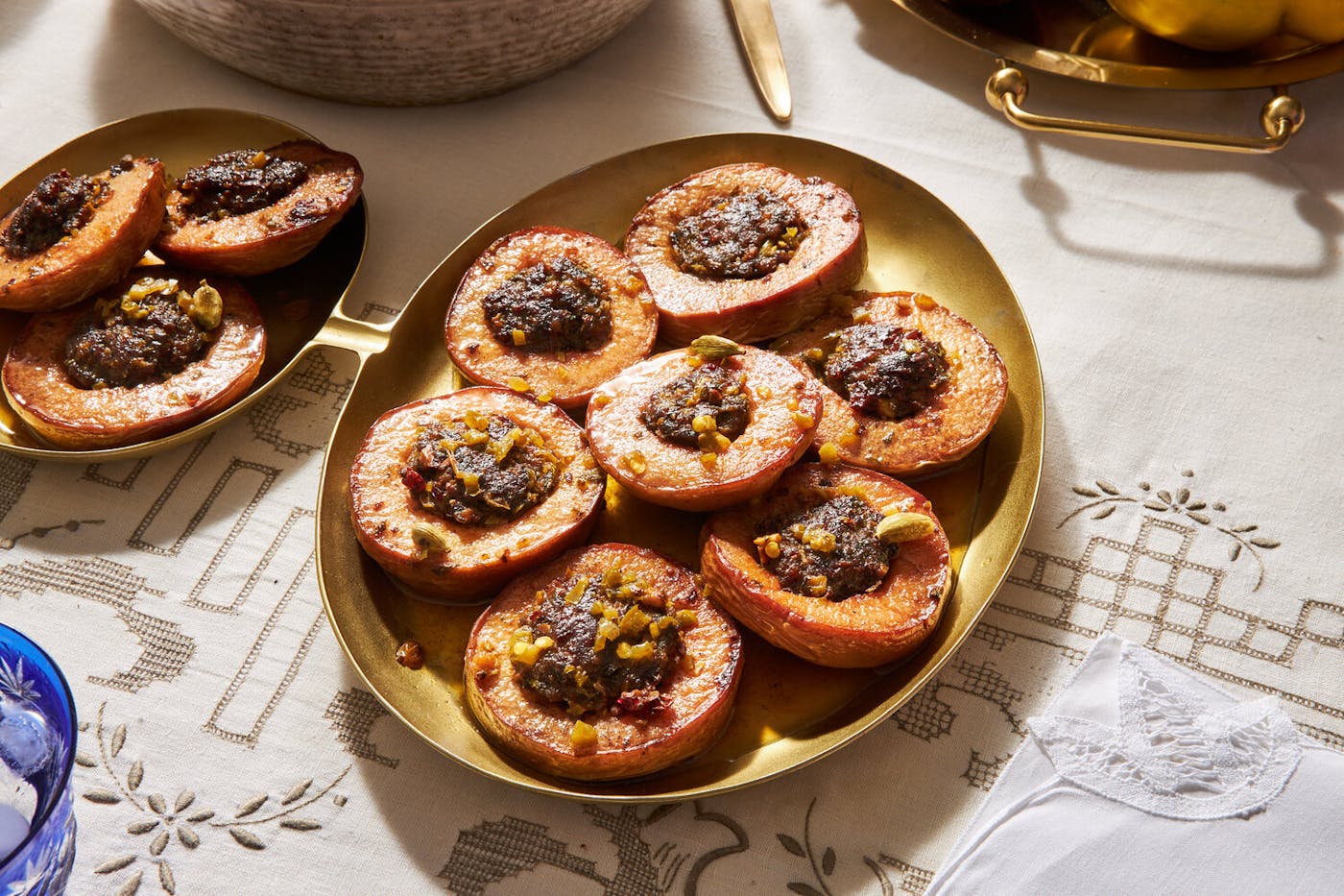 Dolmeh beh on gold platter with platter of fresh quince atop white patterned tablecloth.