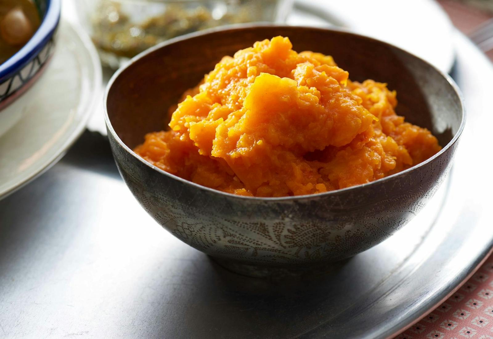 Mashed pumpkin in textured bowl on large tray, atop pink tablecloth.