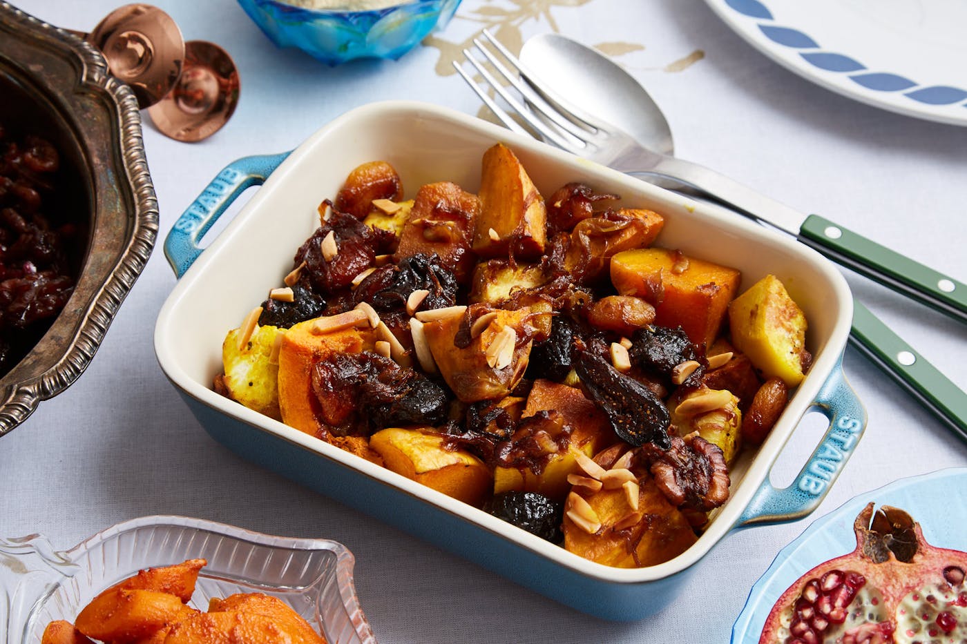 Veggie tanzia with slivered almonds in white and blue casserole dish alongside fresh pomegranate.