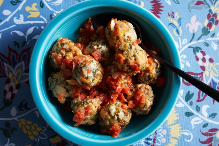 Fish albondigas with tomato sauce in blue bowl atop blue floral tablecloth.