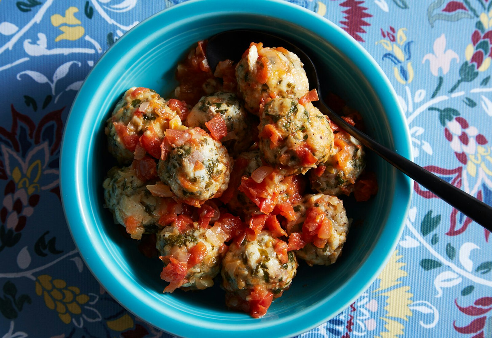 Fish albondigas with tomato sauce in blue bowl atop blue floral tablecloth.