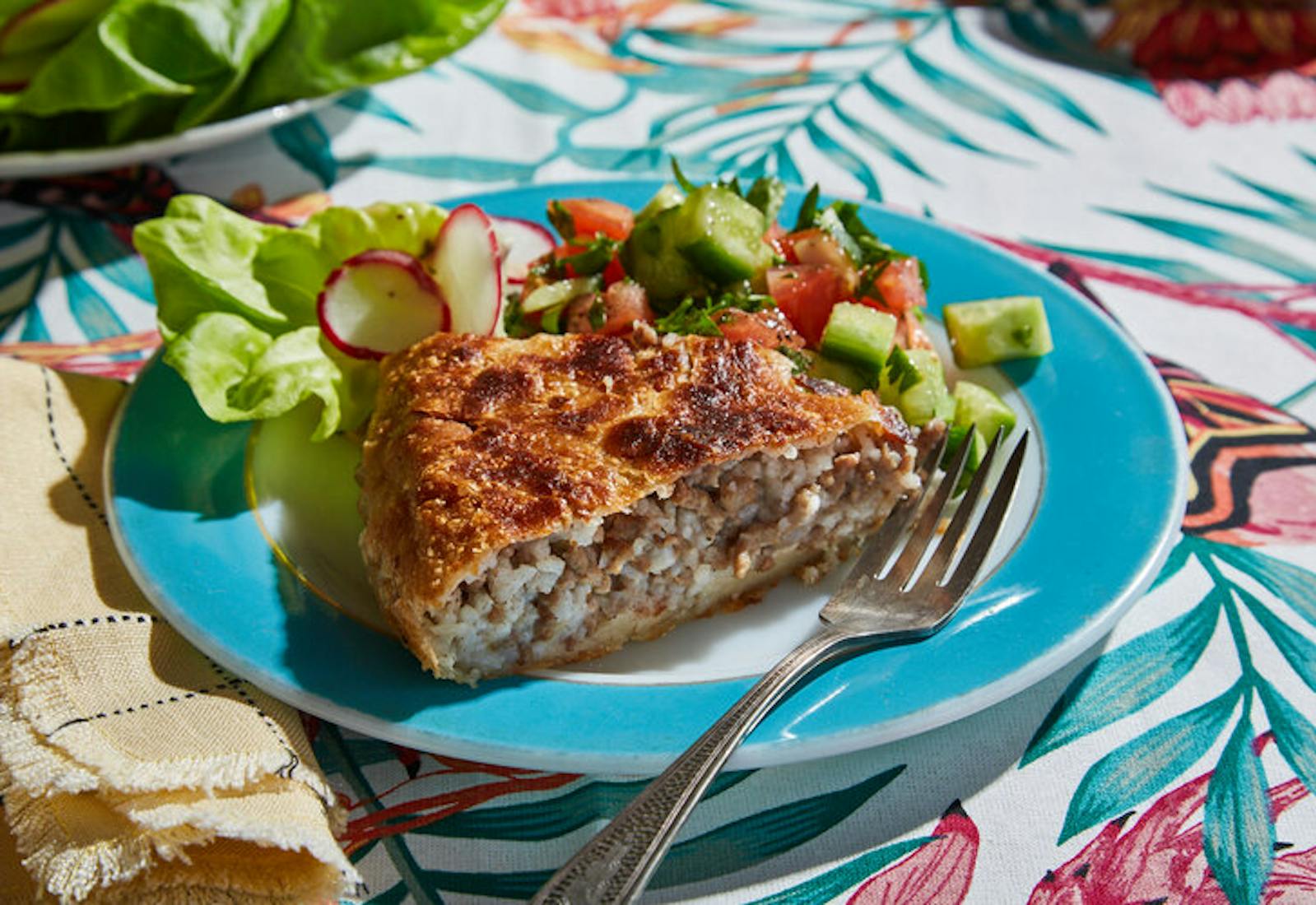 Slice of pastel with side of salad on blue plate atop vibrant nature-patterned tablecloth.