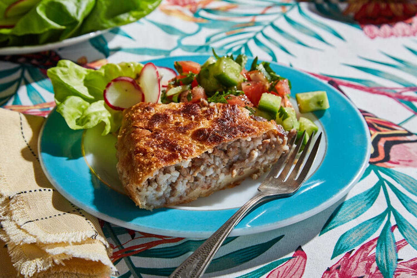 Slice of pastel with side of salad on blue plate atop vibrant nature-patterned tablecloth.